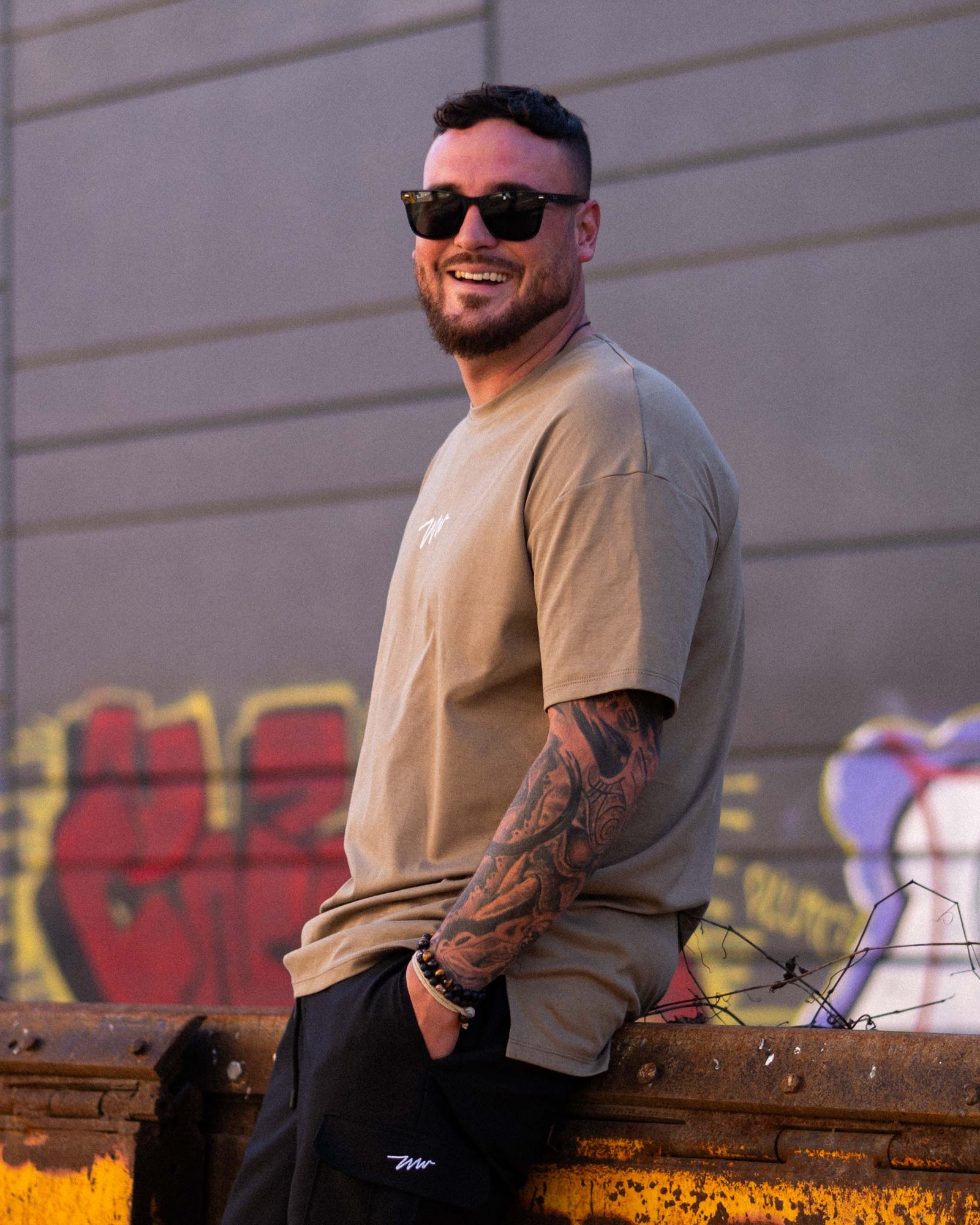 Tall male model wearing a kaki Wadlow t-shirt and black pants, outdoor street style shoot. Premium clothing for tall men made in Canada.