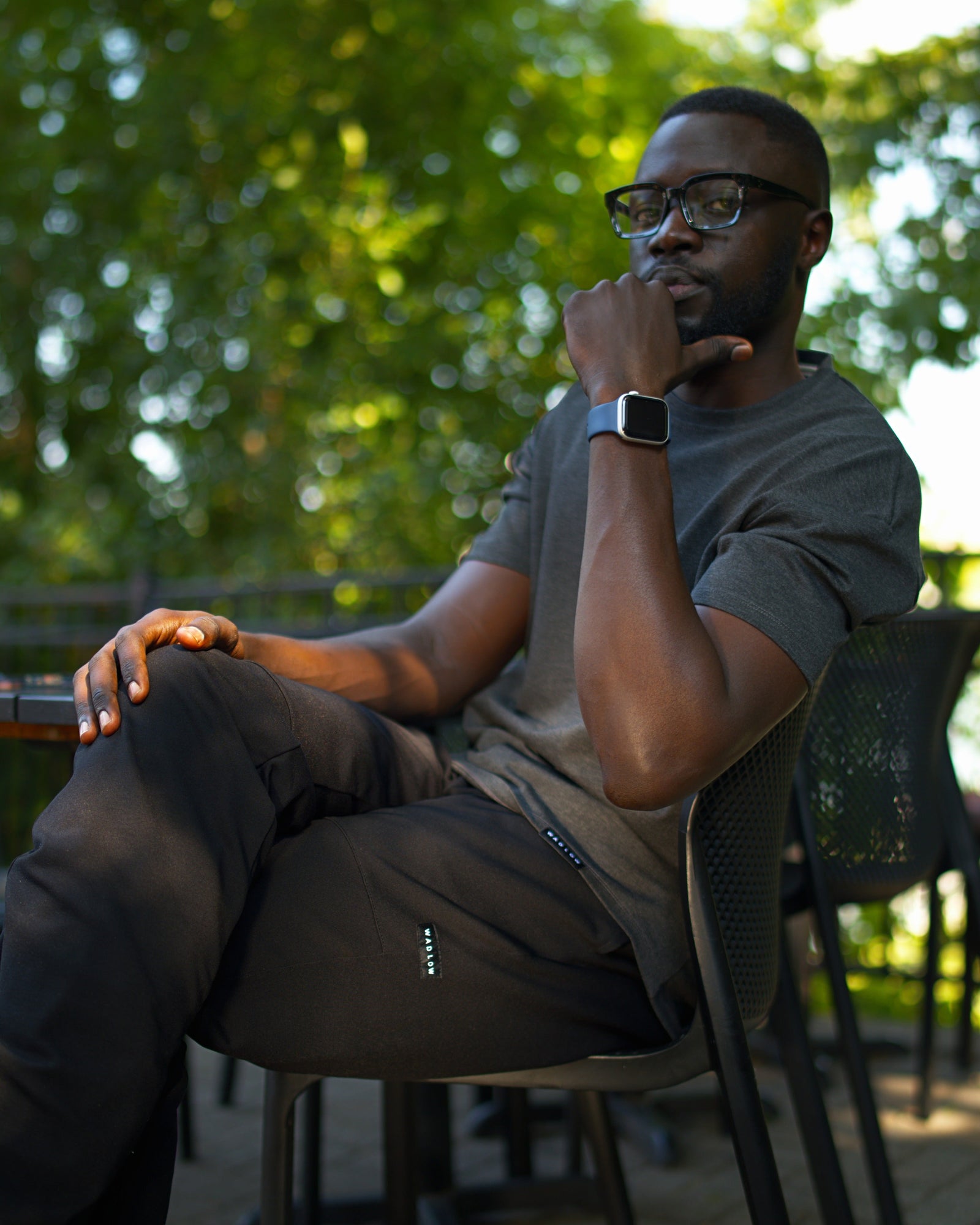 Tall man wearing black Wadlow Tall Set Pants and a dark grey Pon'tee, sitting outdoors.