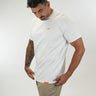 A man wearing a tall white short-sleeve crewneck t-shirt with a small orange logo on the left chest, paired with beige tall 36 inseam pants