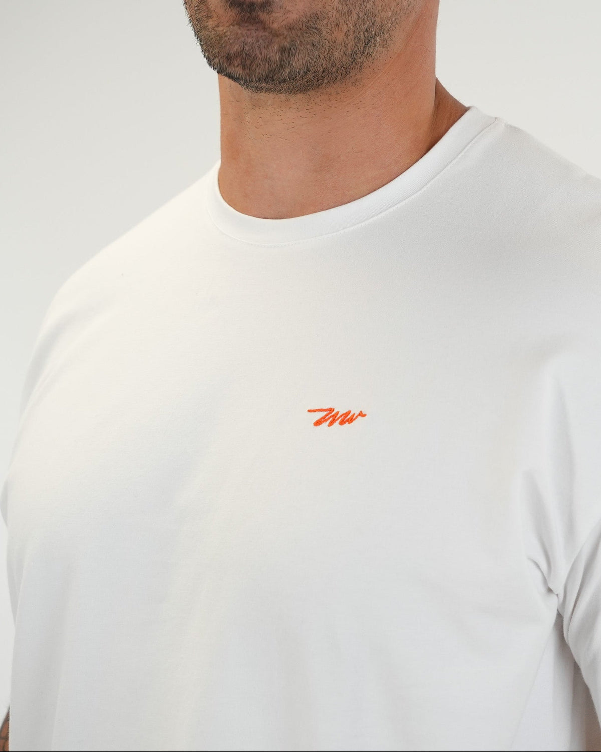 Close-up of a tall man wearing a white crewneck t-shirt with a small orange embroidered Wadlow logo on the chest.